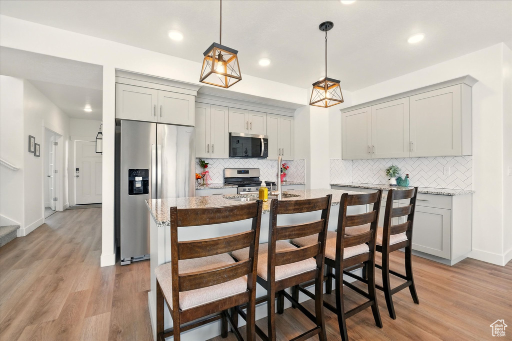 Kitchen featuring appliances with stainless steel finishes, gray cabinets, backsplash, light wood-type flooring, and pendant lighting