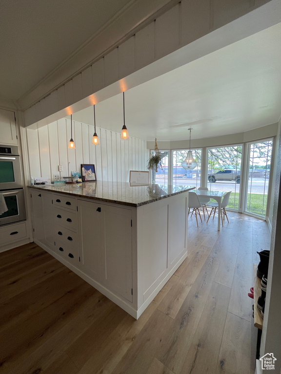 Kitchen featuring stainless steel double oven, light wood finished floors, light stone countertops, and white cabinets