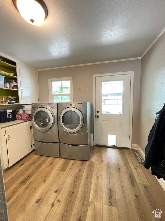 Laundry area with cabinet space, washer and clothes dryer, light wood finished floors, ornamental molding, and a textured ceiling