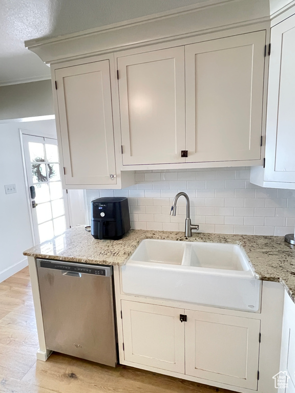 Kitchen featuring stainless steel dishwasher, a sink, tasteful backsplash, light wood-type flooring, and white cabinetry