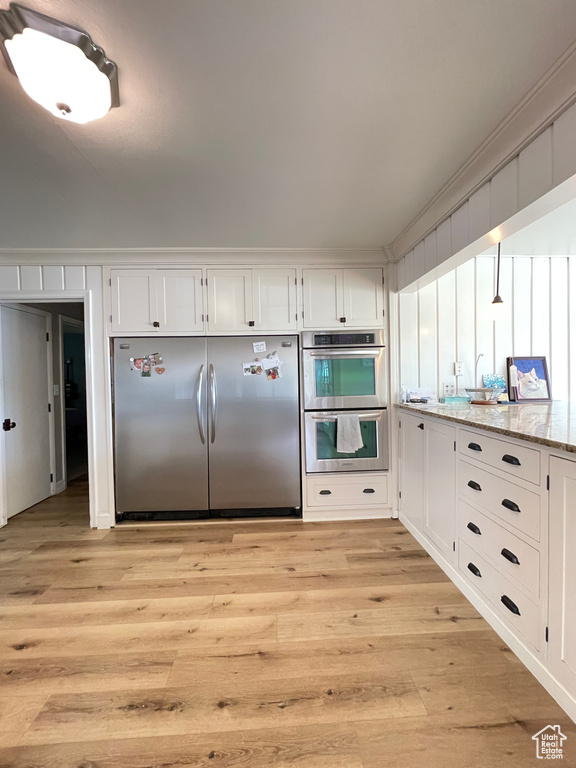 Kitchen featuring appliances with stainless steel finishes, light wood-style floors, white cabinets, and light stone countertops