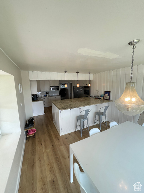 Kitchen featuring stainless steel appliances, light wood-style floors, decorative light fixtures, white cabinetry, and a breakfast bar area