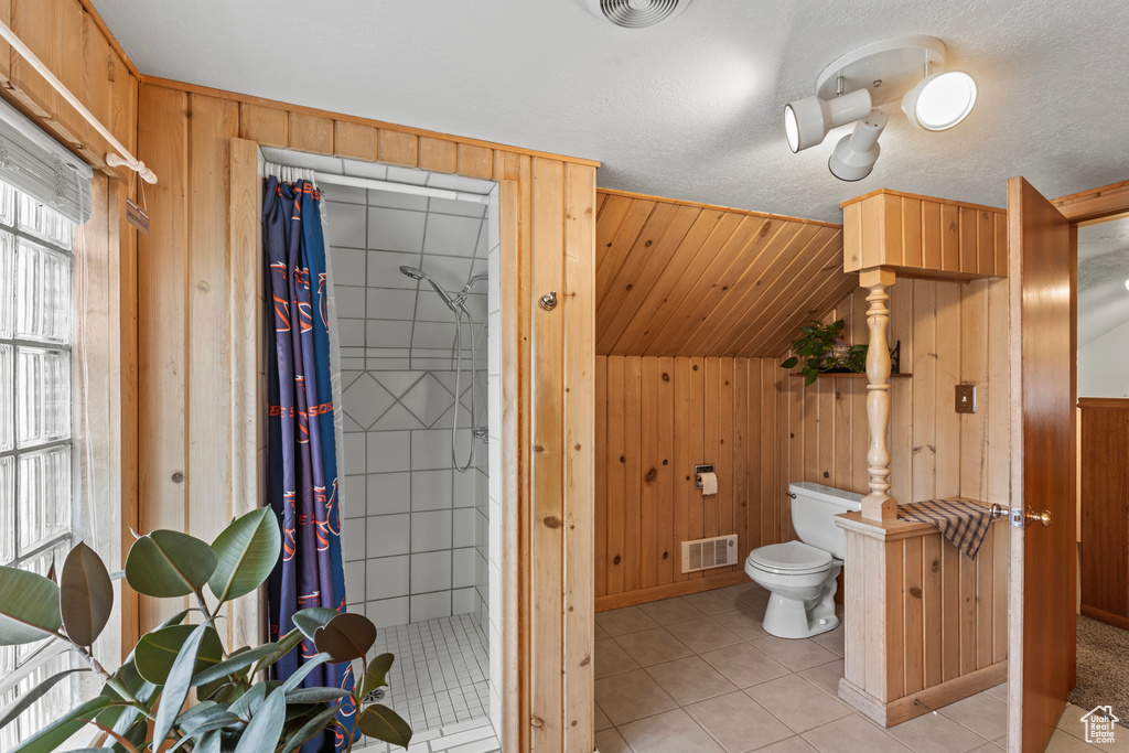 Bathroom with wood walls, a stall shower, toilet, and tile patterned floors