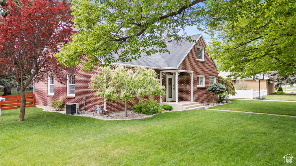 View of front of house with central AC unit, a shingled roof, and brick siding