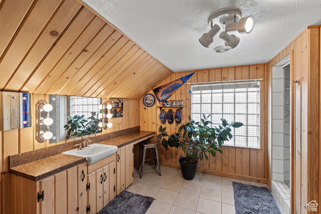 Kitchen with a sink, dark countertops, vaulted ceiling, wooden walls, and light tile patterned floors