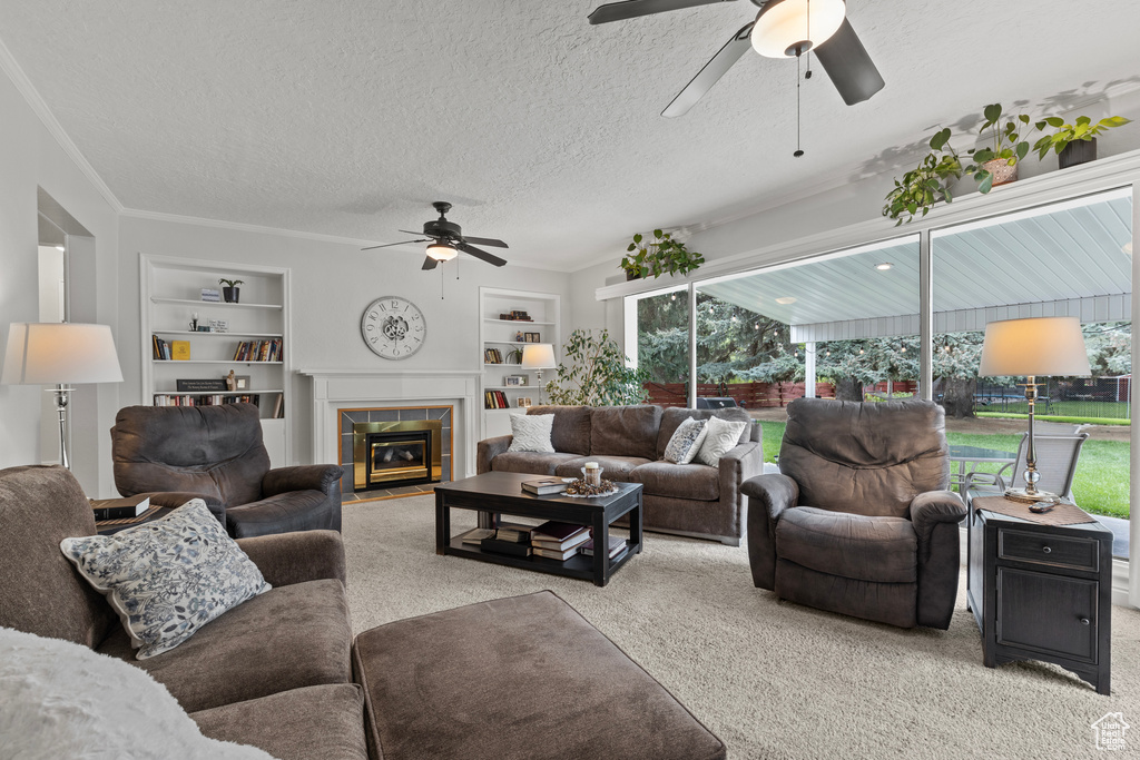 Carpeted living area with a ceiling fan, built in shelves, a tile fireplace, and a textured ceiling