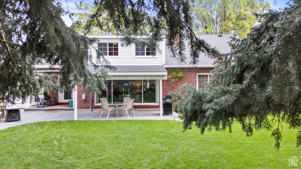 Rear view of house featuring brick siding, a patio, and a yard