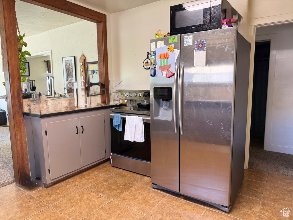 Kitchen featuring stainless steel appliances, light tile patterned floors, dark countertops, and white cabinetry