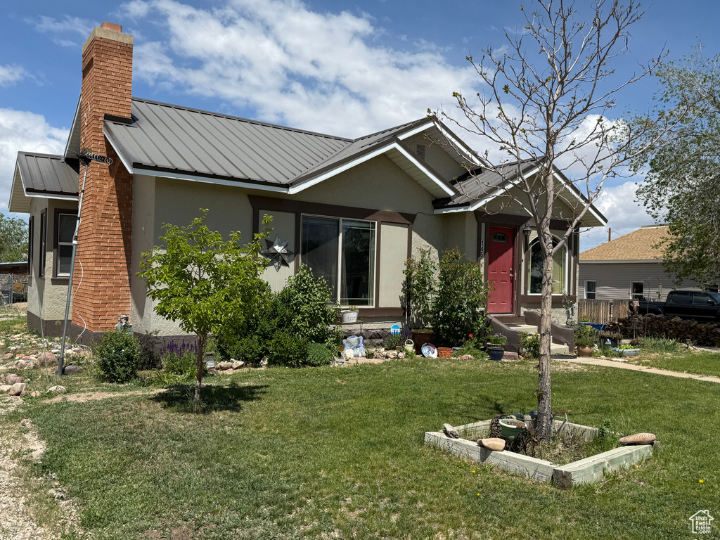 Ranch-style home with a chimney, stucco siding, a front yard, metal roof, and a standing seam roof