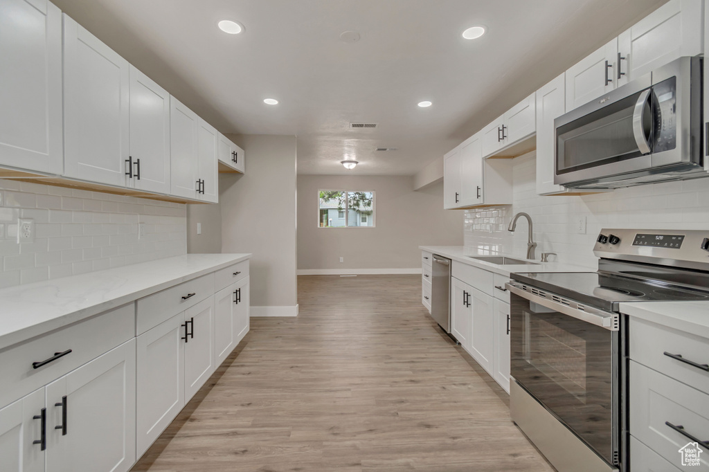 Kitchen featuring stainless steel appliances, a sink, baseboards, recessed lighting, and light wood finished floors