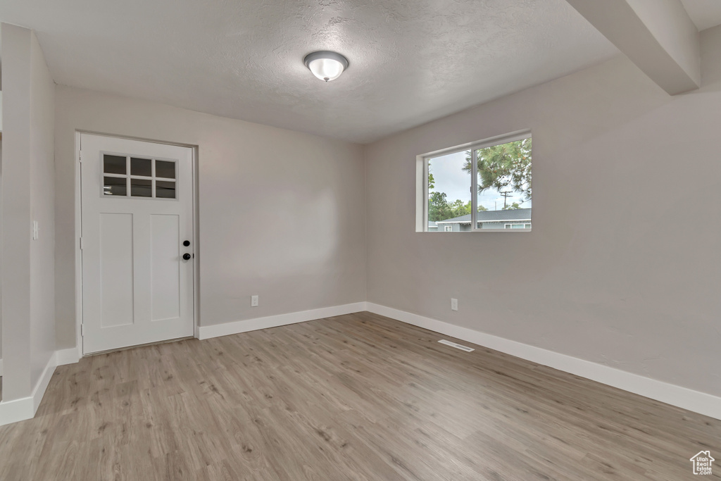 Empty room with light wood-type flooring, baseboards, and a textured ceiling