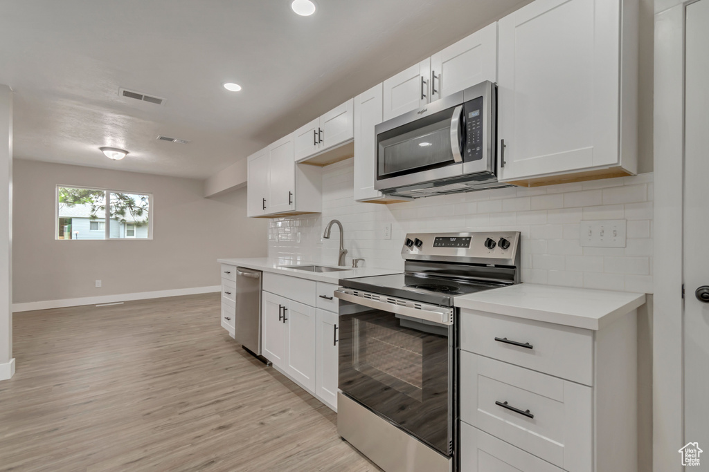 Kitchen with appliances with stainless steel finishes, a sink, baseboards, light countertops, and recessed lighting
