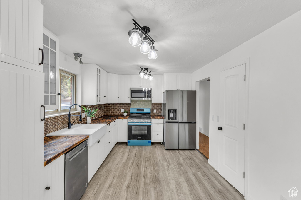 Kitchen featuring stainless steel appliances, wood counters, backsplash, a sink, and light wood finished floors