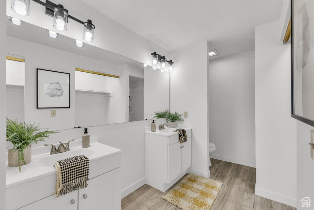 Bathroom with two vanities, toilet, wood finished floors, and baseboards