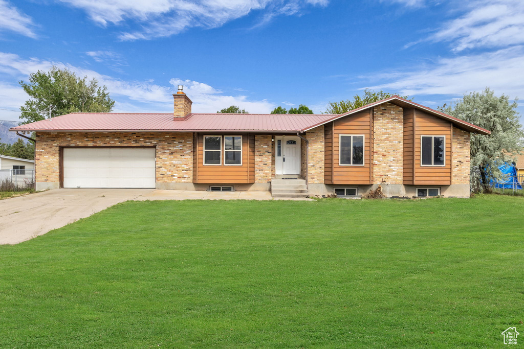 View of front of home with driveway, a chimney, a front yard, an attached garage, and metal roof
