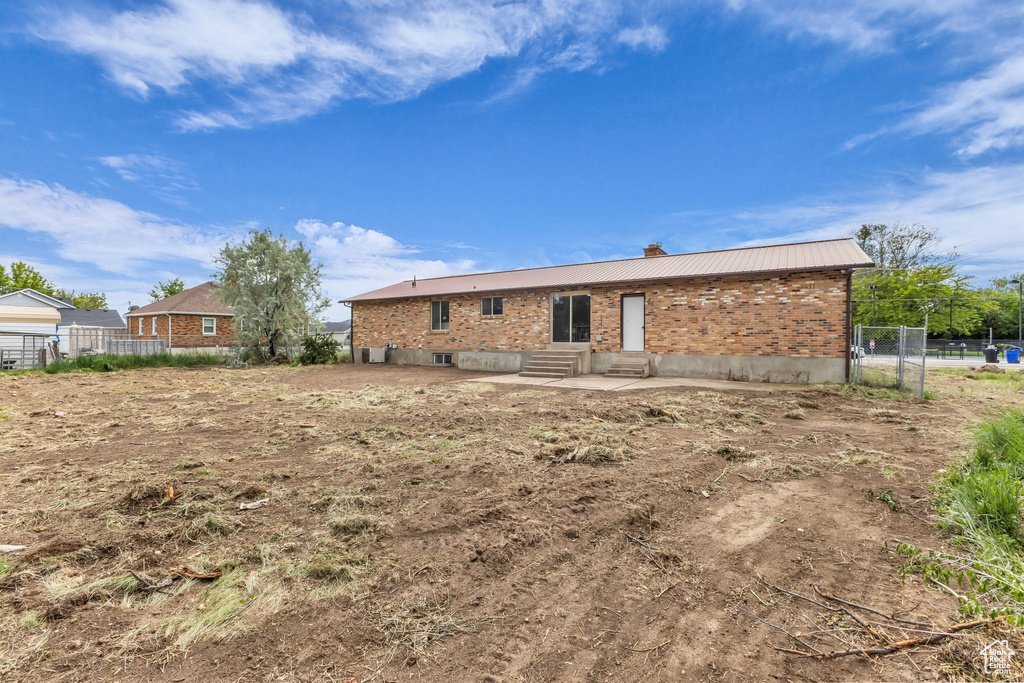 Back of house with entry steps, a chimney, brick siding, metal roof, and a patio area