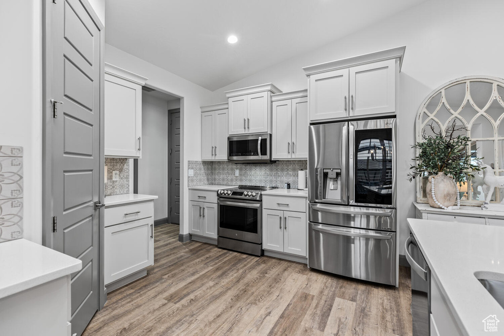 Kitchen featuring appliances with stainless steel finishes, light countertops, vaulted ceiling, decorative backsplash, and light wood-style floors