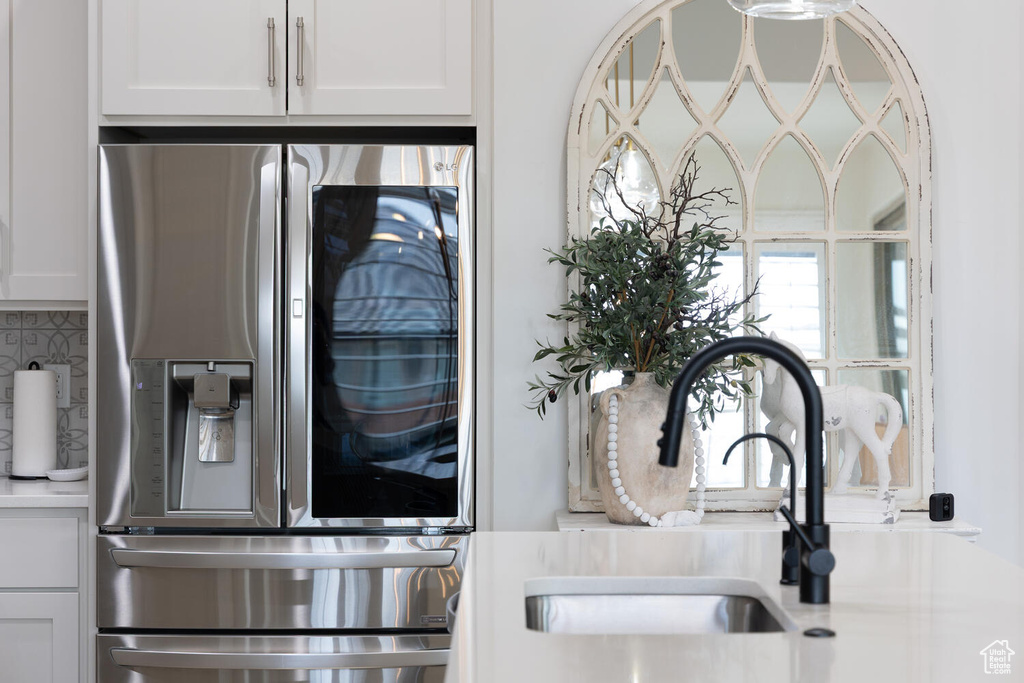 Kitchen view of stainless steel fridge, a sink, tasteful backsplash, light countertops, and white cabinets