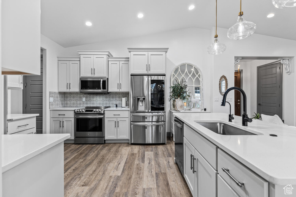 Kitchen with stainless steel appliances, a sink, vaulted ceiling, light countertops, and tasteful backsplash
