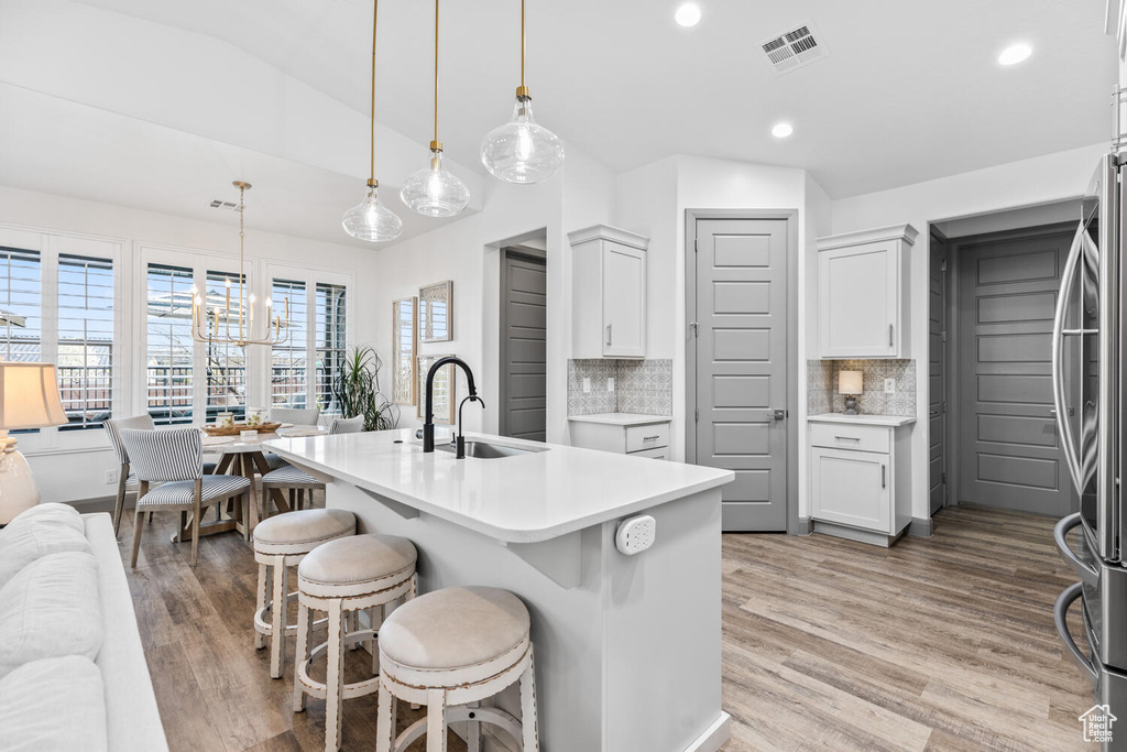 Kitchen with a sink, freestanding refrigerator, light countertops, a kitchen breakfast bar, and backsplash