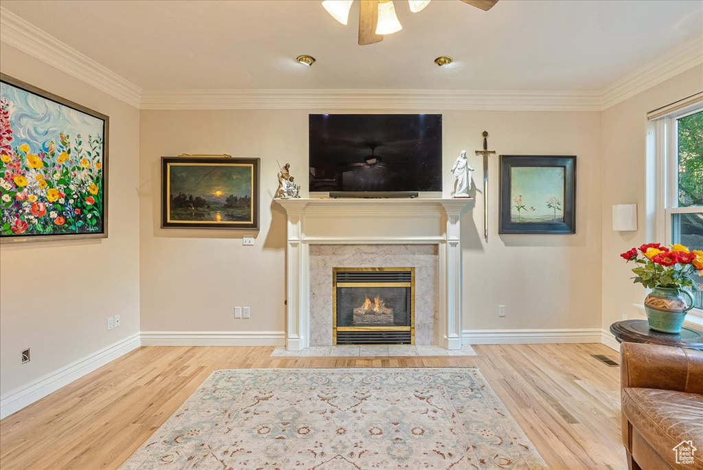 Living area with crown molding, a fireplace, a ceiling fan, baseboards, and wood finished floors