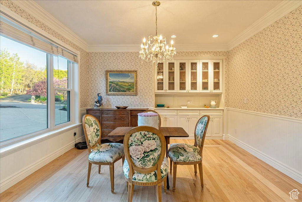 Dining room with a notable chandelier, a wainscoted wall, wallpapered walls, light wood-type flooring, and ornamental molding
