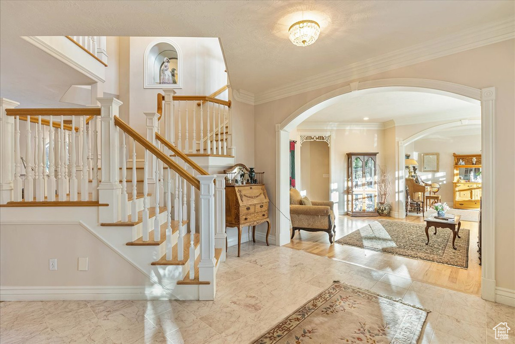 Foyer featuring crown molding, arched walkways, baseboards, marble finish floor, and stairs