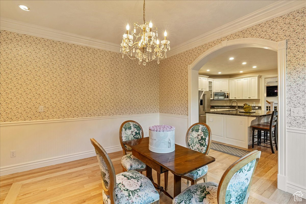 Dining room with arched walkways, a chandelier, light wood-style flooring, a wainscoted wall, and wallpapered walls