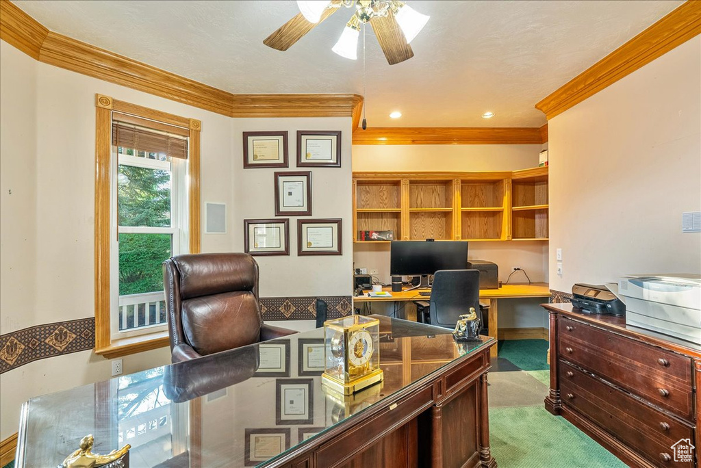 Carpeted home office with crown molding, built in desk, and ceiling fan