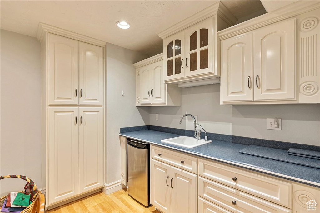 Kitchen with dark countertops, a sink, dishwasher, light wood-type flooring, and glass insert cabinets