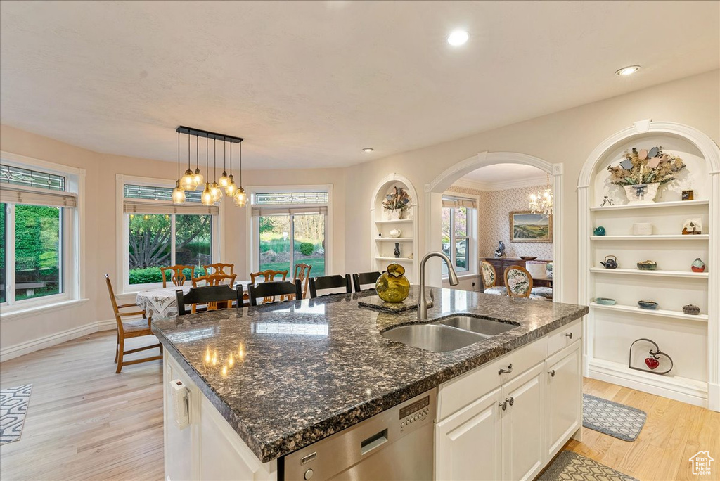 Kitchen with a healthy amount of sunlight, a kitchen island with sink, stainless steel dishwasher, light wood-type flooring, and a sink