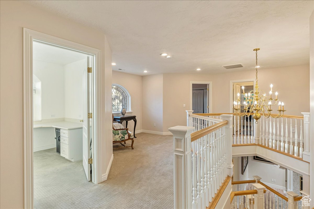 Hall with visible vents, light carpet, baseboards, a chandelier, and an upstairs landing