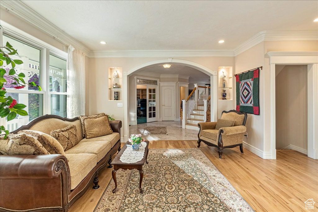 Living room featuring arched walkways, ornamental molding, and light wood finished floors