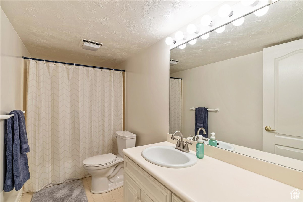 Full bathroom with tile patterned flooring, visible vents, vanity, toilet, and a textured ceiling
