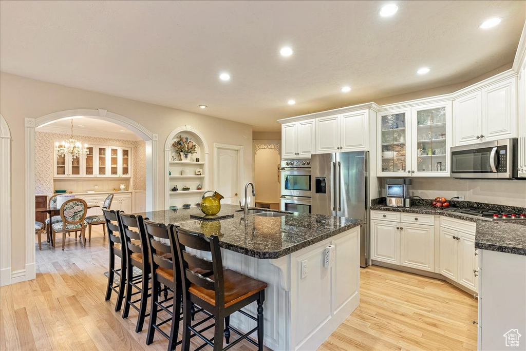 Kitchen featuring a breakfast bar area, appliances with stainless steel finishes, arched walkways, light wood-type flooring, and a sink