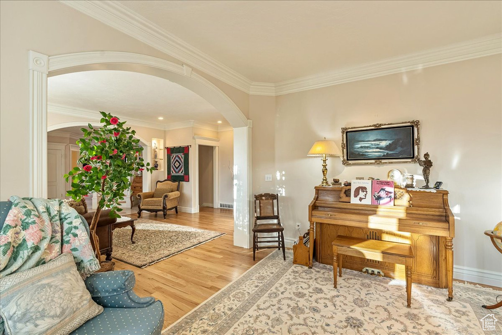 Living area featuring crown molding, arched walkways, baseboards, and wood finished floors