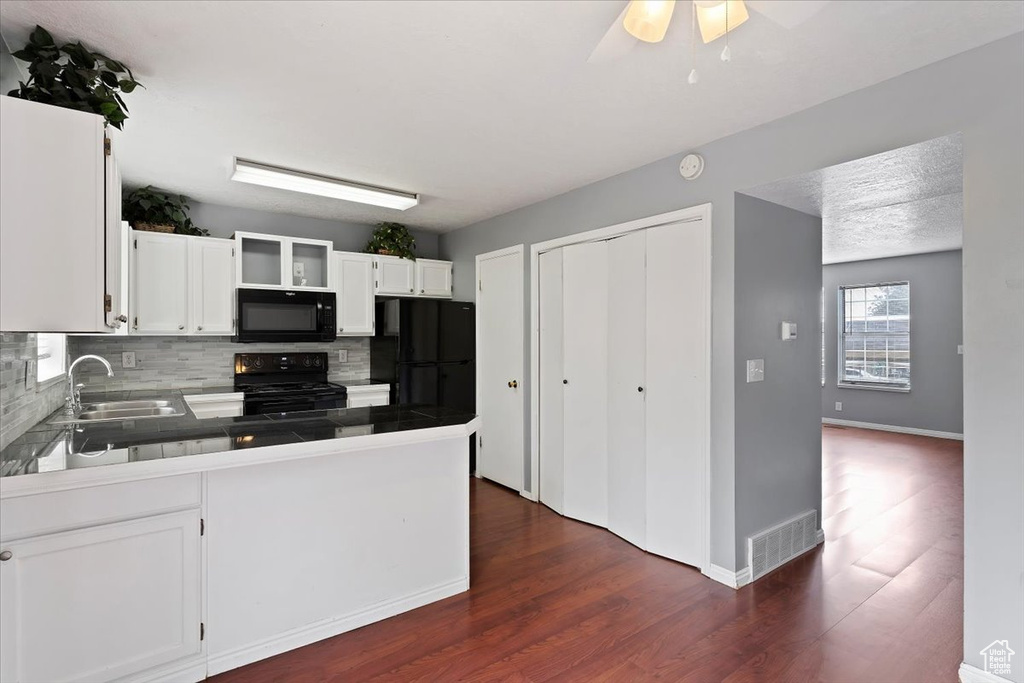 Kitchen featuring black appliances, a sink, backsplash, a peninsula, and white cabinetry