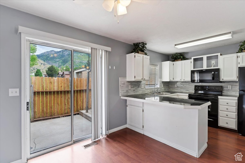 Kitchen with black appliances, white cabinets, a sink, a peninsula, and dark wood-type flooring