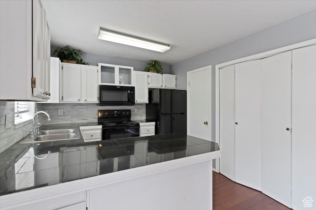 Kitchen featuring black appliances, a peninsula, a sink, dark countertops, and backsplash