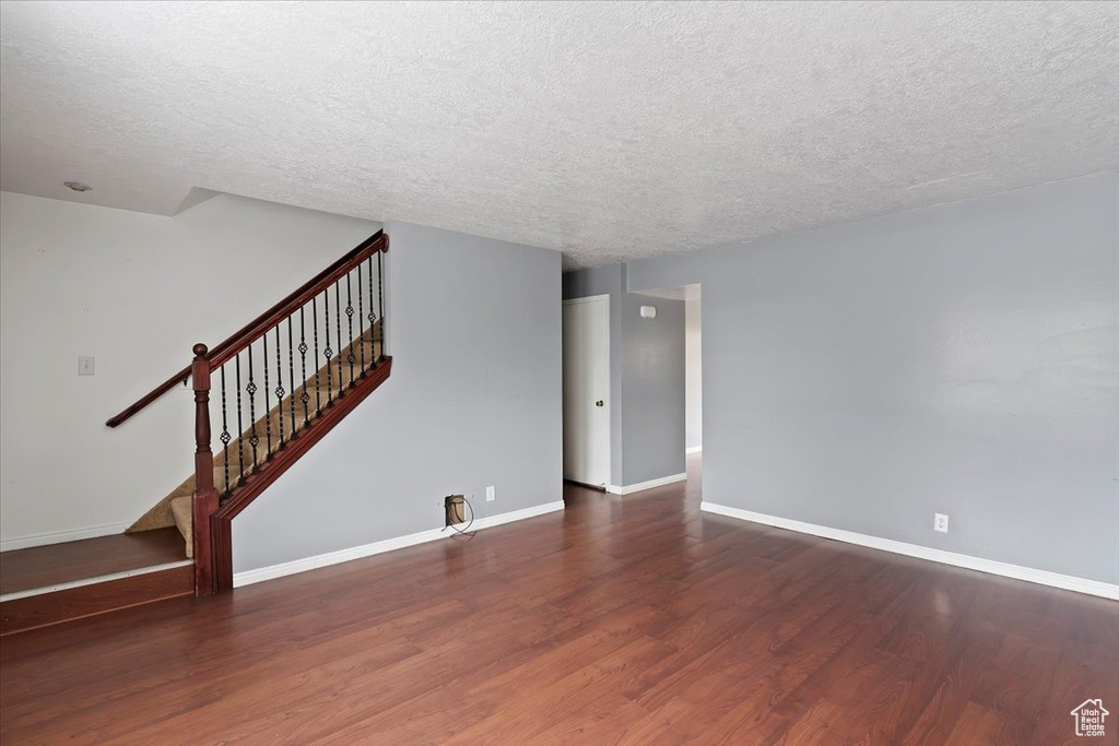 Unfurnished living room with a textured ceiling, wood finished floors, baseboards, and stairs