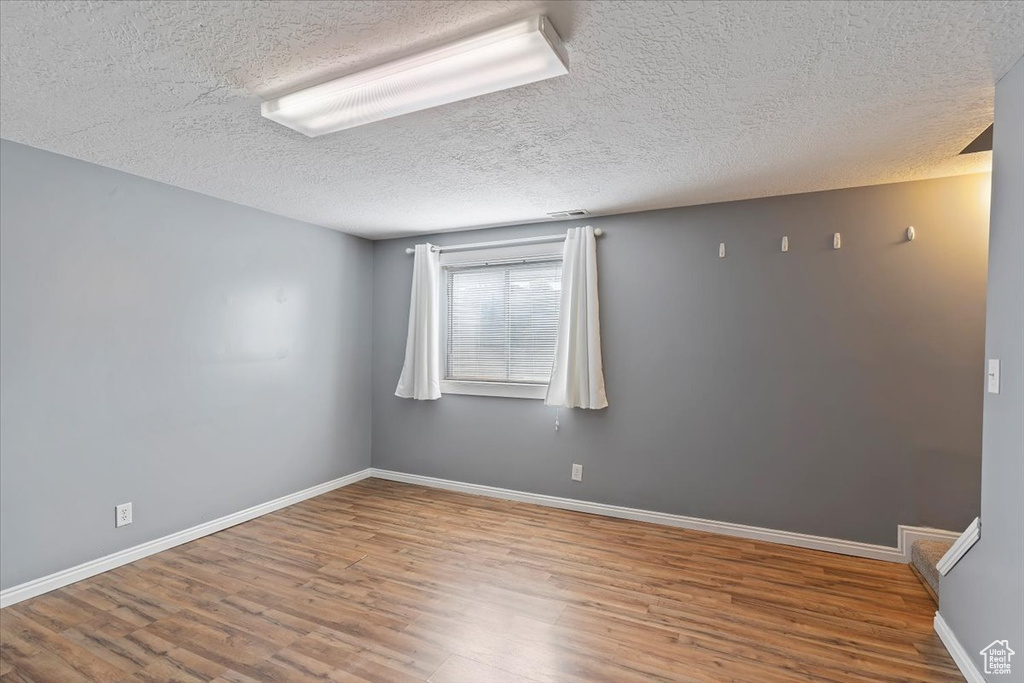 Spare room featuring wood finished floors, a textured ceiling, and baseboards