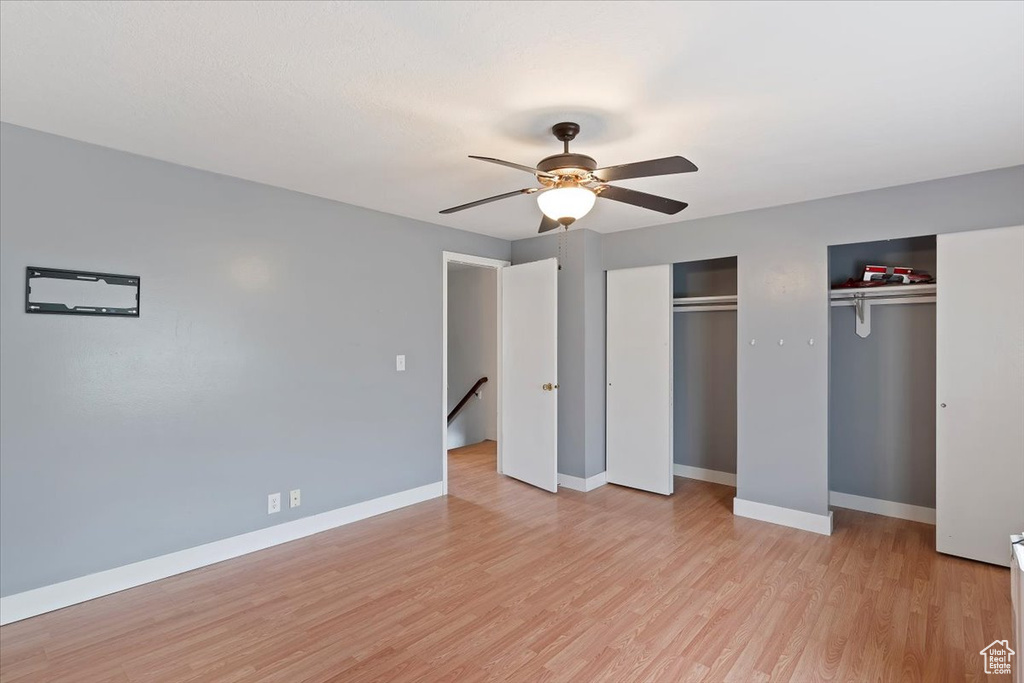Unfurnished bedroom with two closets, light wood-style floors, baseboards, and ceiling fan