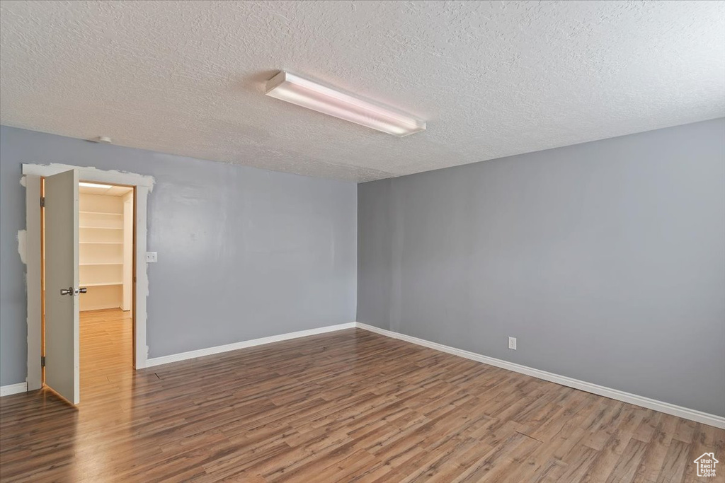 Empty room featuring wood finished floors, a textured ceiling, and baseboards