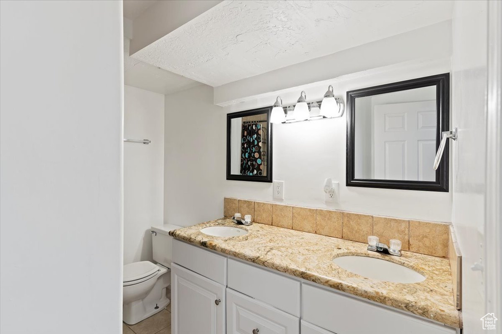 Bathroom with toilet, double vanity, tile patterned floors, and a textured ceiling
