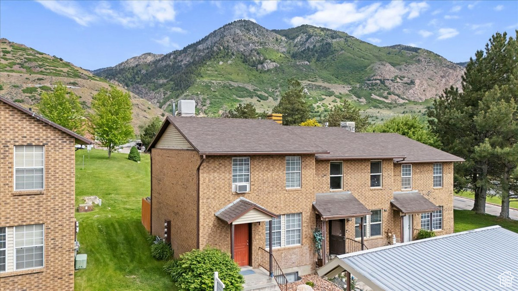 View of front of property with a mountain view, a front lawn, brick siding, cooling unit, and a chimney