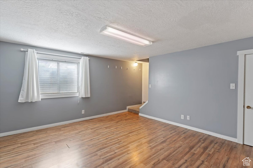 Empty room with wood finished floors, a textured ceiling, and baseboards