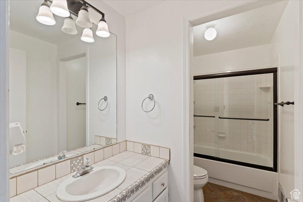 Bathroom featuring toilet, vanity, combined bath / shower with glass door, and tile patterned floors