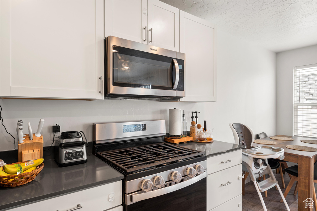 Kitchen with appliances with stainless steel finishes, dark countertops, white cabinetry, and a textured ceiling