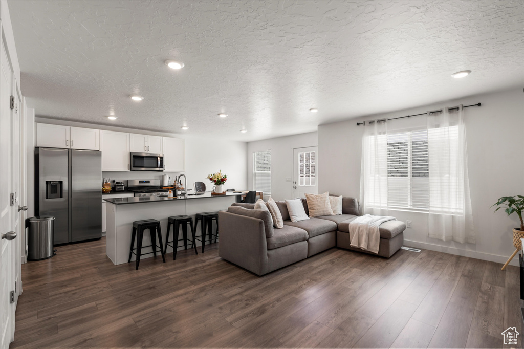 Living area featuring recessed lighting, dark wood-style flooring, a textured ceiling, and baseboards