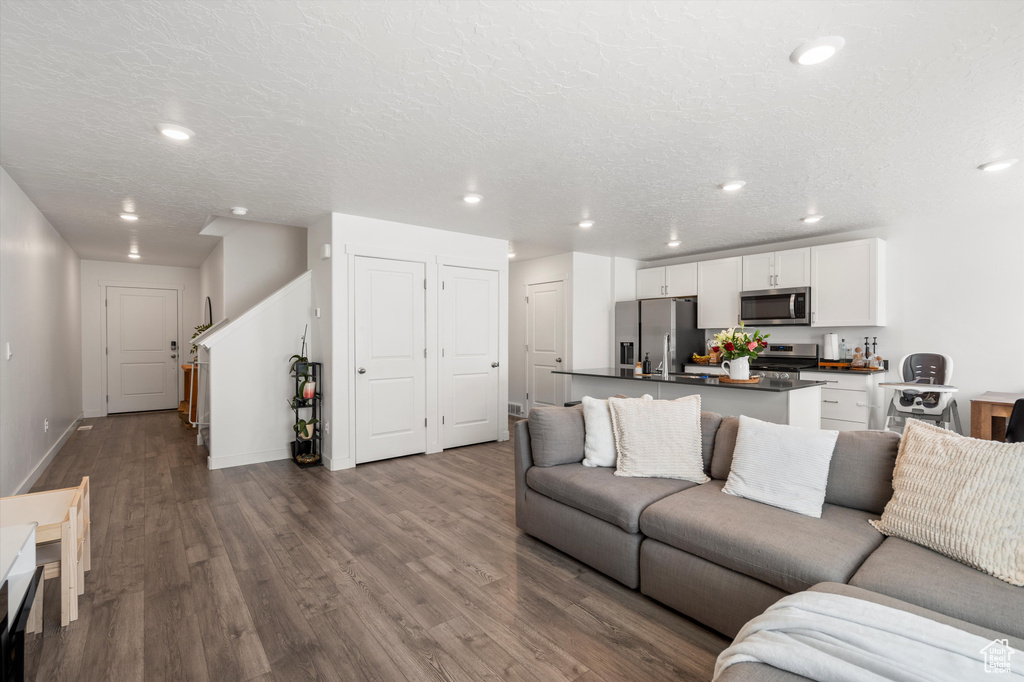 Living area with dark wood-type flooring, recessed lighting, baseboards, and a textured ceiling